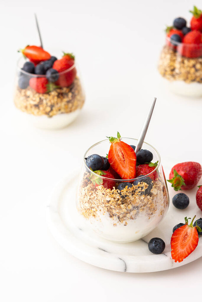 Házi készítésű granola mandulával egy pohár joghurttal, friss eper és áfonya, finom egészséges reggeli - Fotó, kép