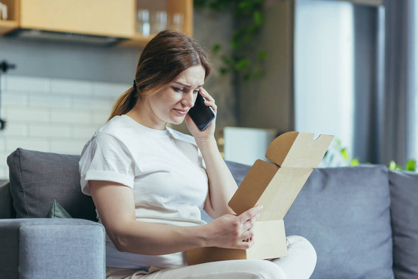 Pregnant woman at home angry and disappointed received the wrong parcel, a woman on the couch talking on the phone - Photo, image