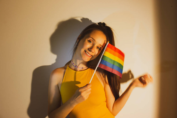 Красива молода жінка, дівчинка тримає ЛГБТ-прапор в руці, відзначаючи День Гордості. Мила сексуальна дівчина має задоволення, посмішку, сміх. Прапор веселки - символ лесбіянок, бісексуалів, пансексуалів, геїв. Виходь.. - Фото, зображення