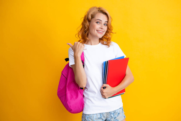 Portrait of happy woman holding backpack. Study process. Young cute student girl with backpack holds some documents and books over yellow background - 写真・画像
