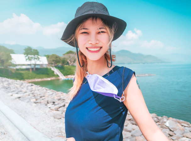 Asian woman with hat and summer wear is taking portrait while on vacation at the beach. - 写真・画像