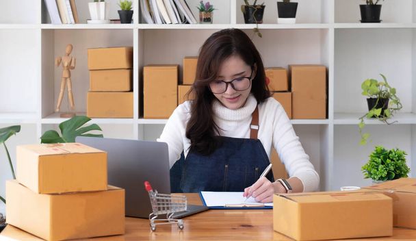 Young beautiful happy asian business woman owner of SME online using laptop receive order from customer with parcel box packaging at her startup home office, online business seller and deliver - Fotoğraf, Görsel
