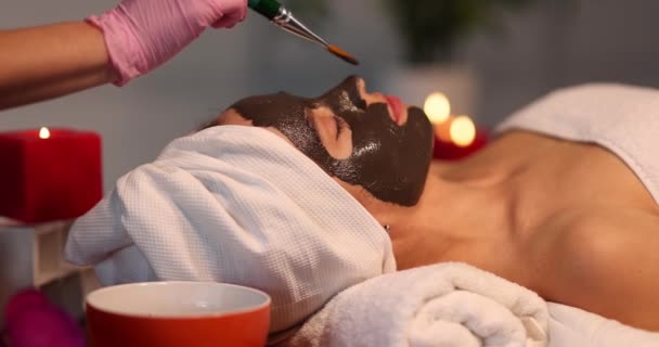 L'estetista spalma la maschera cosmetica su faccia di una donna in salone. Trattamenti viso anti-invecchiamento concetto - Filmati, video
