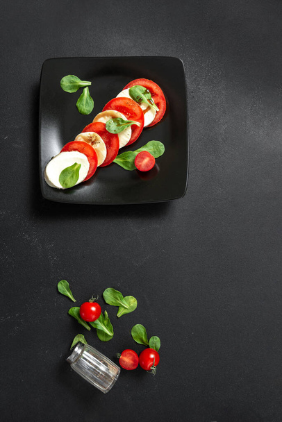Klassischer italienischer Salat mit Mozzarella und Tomaten auf schwarzem Teller. Salat Caprese vorhanden. Senkrechtstarter - Foto, Bild