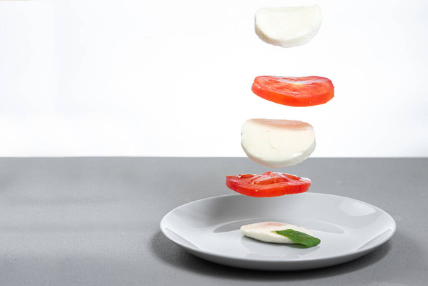 A Caprese saláta egy olasz klasszikus. Összetevők sajt és paradicsom repül a levegőben - Fotó, kép