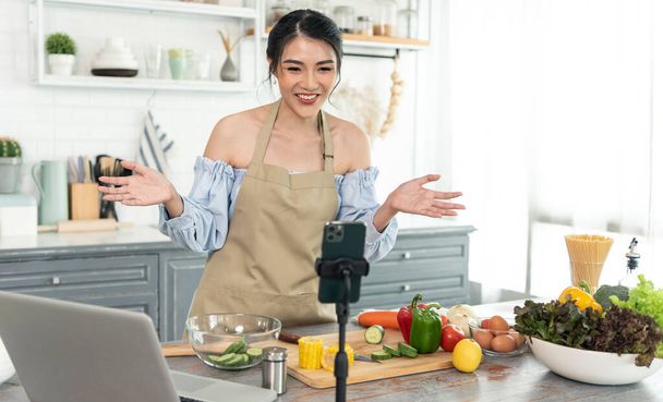 Asijské žena jídlo blogger vaření salát v přední části smartphone kamery při nahrávání vlog videa a živé streamování doma v kuchyni.  - Fotografie, Obrázek