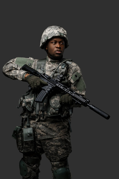 Taisteleva afrikkalainen sotilas, jolla on vakava kasvojen pitelykivääri, katsoo pois tummaa taustaa vasten. - Valokuva, kuva