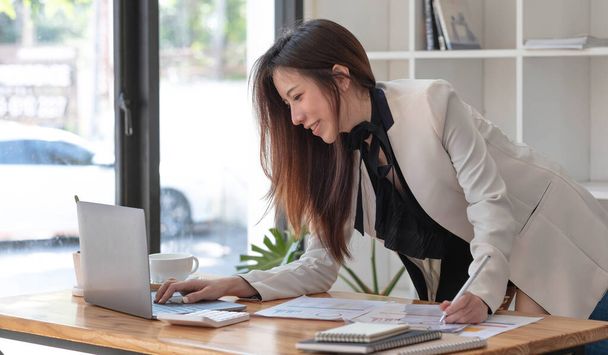 Счастливая молодая азиатская бизнесвумен, стоящая в офисе за ноутбуком - Фото, изображение