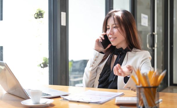 Feliz joven empresaria asiática usando teléfono inteligente y computadora portátil en la oficina - Foto, Imagen