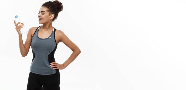 Zdrowie i Fitness koncepcja - piękne African American girl w sporcie ubrania plastikowe butelki wody w gospodarstwie po treningu. Na białym tle na tle białego studia. - Zdjęcie, obraz