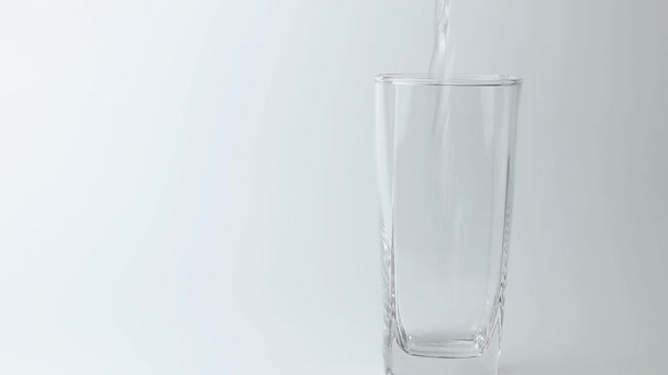 χύνοντας το ποτό γλυκού νερού στο ποτήρι σε γκρι φόντο. Χυνόμενο νερό - Πλάνα, βίντεο