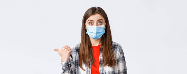 Coronavirus outbreak, leisure on quarantine, social distancing and emotions concept. Astonished and impressed cute woman in medical mask showing way, talking about banner on left side. - Photo, image