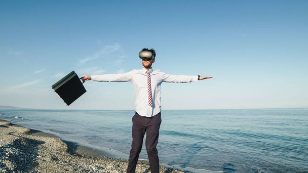 Biznesmen obraca się w okularach wirtualnej rzeczywistości na plaży nad morzem. Statyczne pędy. - Zdjęcie, obraz
