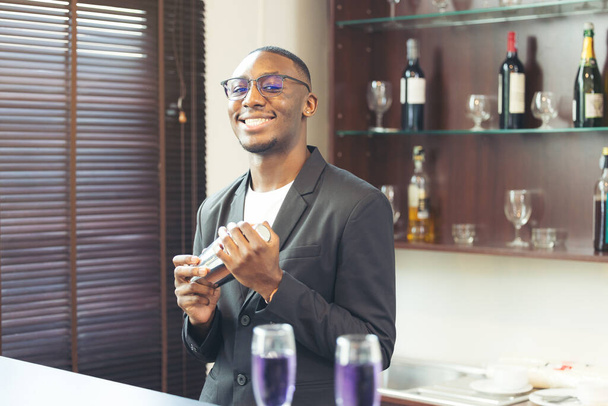 Делая напиток, черный красивый бармен улыбается в камеру. - Фото, изображение
