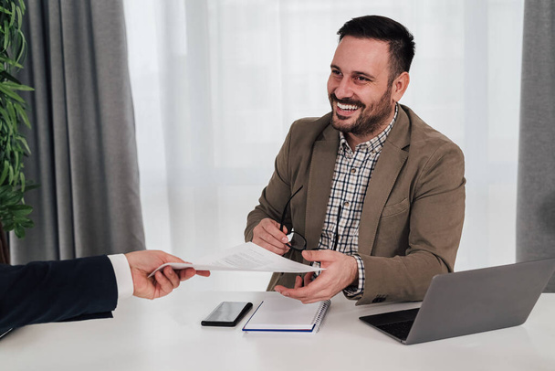 Executive giving contract to smiling businessman. Male partners in formals discussing in meeting at desk. They are working in corporate office. - Fotoğraf, Görsel