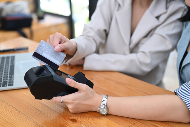 Zugeschnittene Aufnahme zweier Kundin, die eine Kreditkarte durch das Zahlungsterminal streicht. - Foto, Bild