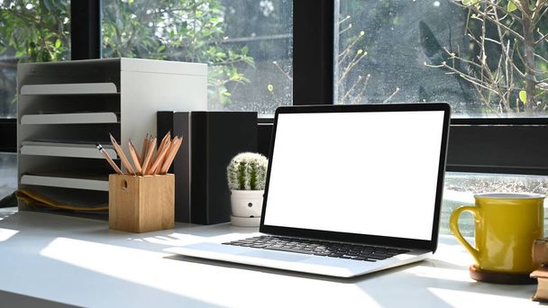 Computador portátil, xícara de café e vaso planta na mesa branca no escritório em casa. Tela em branco para publicidade. - Foto, Imagem