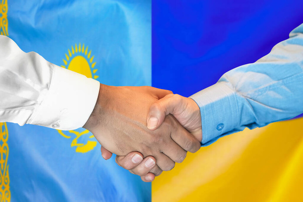 Stretta di mano di affari su sfondo di due bandiere. Gli uomini stringono la mano su sfondo di Kazakistan e bandiera di Ucraina. Concetto di sostegno - Foto, immagini