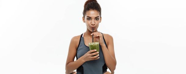gesundes und fittes Konzept - schöne amerikanisch-afrikanische Dame in Fitnessbekleidung, die gesundes Gemüsegetränk trinkt. isoliert auf weißem Hintergrund - Foto, Bild