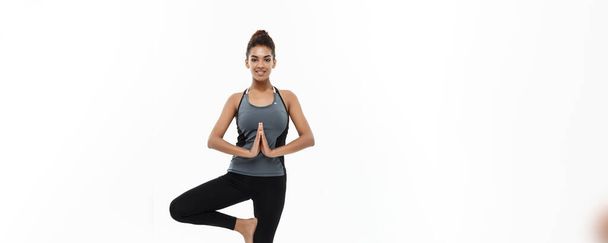 Sağlıklı ve Fitness kavramı - güzel Amerikan Afrika Bayan fitness giyim yoga ve meditasyon yapıyor. Beyaz arka plan üzerinde izole - Fotoğraf, Görsel