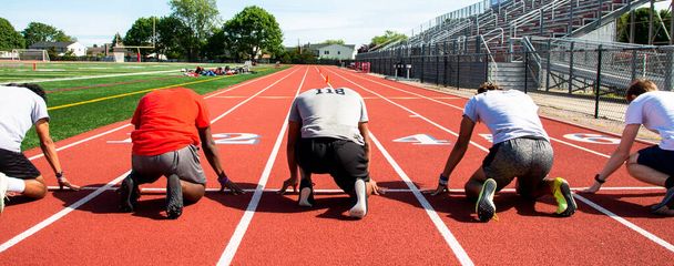 Achteraanzicht van vijf middelbare scholieren in de op uw mark positie in rijstroken op een track klaar om te sprinten en rennen snel. - Foto, afbeelding