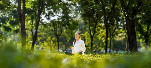 Nainen rentouttavasti harjoittelee meditaatiota metsässä saavuttaakseen onnellisuuden sisäisestä rauhasta viisauden auringonvalolla terveelle mielelle ja sielulle. - Valokuva, kuva