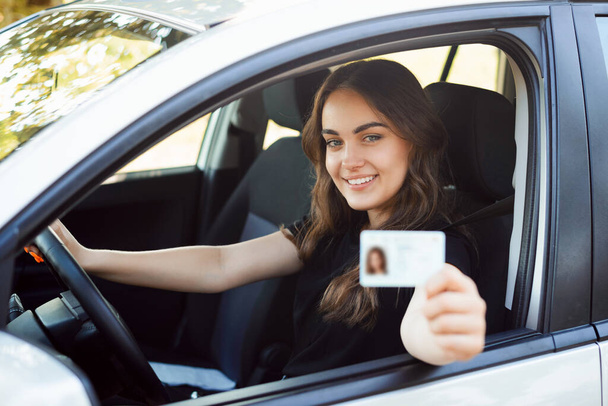 Szczęśliwy kierowca student siedzi w nowoczesnym srebrnym samochodzie i pokazuje prawo jazdy do kamery o dobrym nastroju i chętnie zdać egzaminy na prawo jazdy - Zdjęcie, obraz