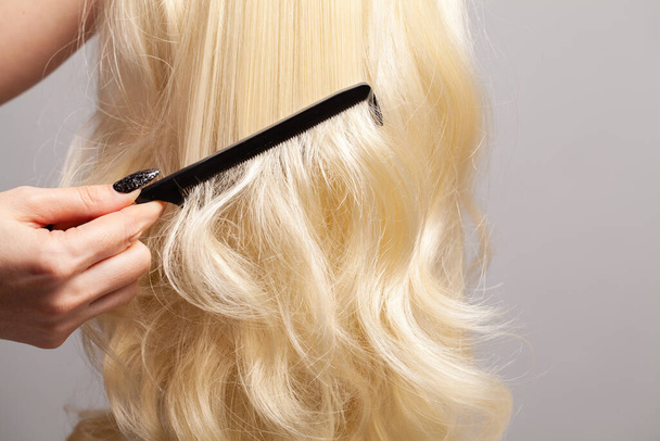 Fryzjer czesanie blond włosy z czarnym plastikowym grzebieniem zbliżenie - Zdjęcie, obraz