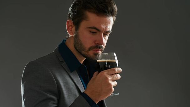 Partial of concentrated caucasian brewer entrepreneur sniffing beer in glass. Bearded man wearing formal wear. Brewing business. Beer tasting. Isolated on grey background. Studio shoot. Copy space - Foto, Bild