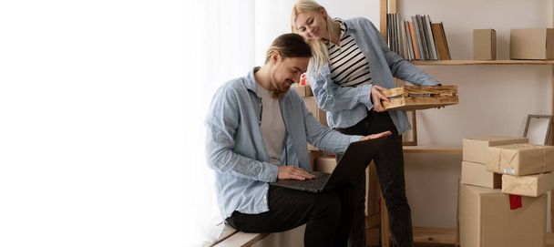 Молодая пара переезжает в новый дом расслабляясь сидя с помощью компьютера ноутбука, улыбаясь счастливы для переезда в новую квартиру, день переезда, баннер, свободное пространство - Фото, изображение