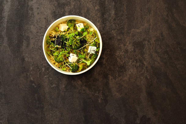 Vegetarian healthy bowl with bulgur, broccoli, greens and feta cheese isolated on dark background. Healthy food delivery service and daily ration concept. - Fotó, kép