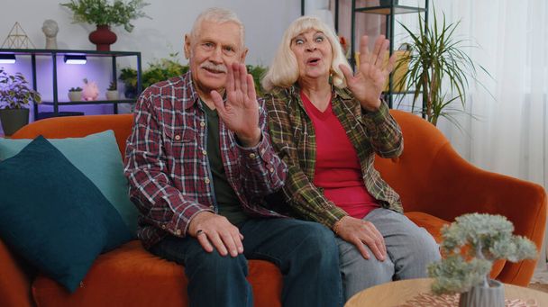 Idős idős család nagyszülők férfi nő mosolyog barátságos a kamera és integetett kezét gesztikuláló hello, hi, üdvözlő vagy viszlát, barátságos kifejezés. Nagymama nagypapa otthon. - Fotó, kép