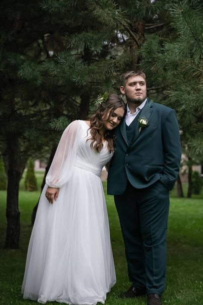 曲線的な人々は、徒歩で結婚式のカップル。スタイリッシュな魅力的な花嫁、緑のスーツの新郎。美しい公園 - 写真・画像