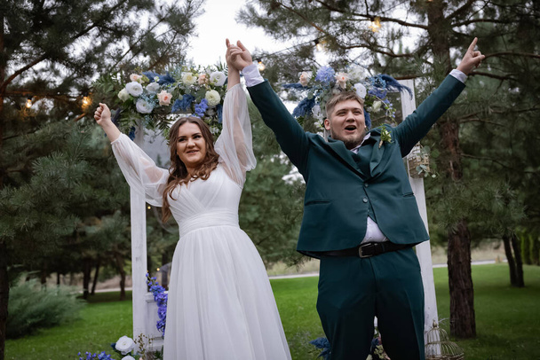 曲線的な人々は、徒歩で結婚式のカップル。スタイリッシュな魅力的な花嫁、緑のスーツの新郎。美しい公園 - 写真・画像