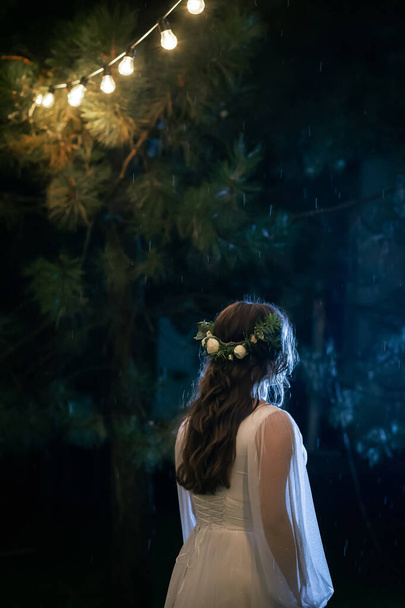 Chica exuberante en un vestido de novia blanco. Elegante novia encantadora y alegre. Parque verde con bombillas en el fondo. - Foto, Imagen