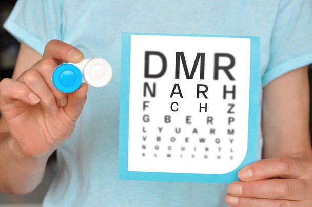 Women holding Contact lens case and snellen eye chart.Medicine and vision concept. Young doctor holding eyesight test chart showing that contact lenses correct vision.Selective focus - Photo, Image