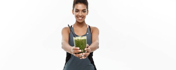 gesundes und fittes Konzept - schöne amerikanisch-afrikanische Dame in Fitnessbekleidung, die gesundes Gemüsegetränk trinkt. isoliert auf weißem Hintergrund - Foto, Bild