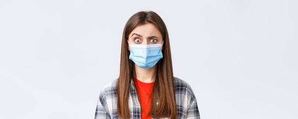 Coronavirus outbreak, leisure on quarantine, social distancing and emotions concept. Confused and startled girl in medical mask seeing something strange, raise eyebrow skeptical. - Foto, Imagem