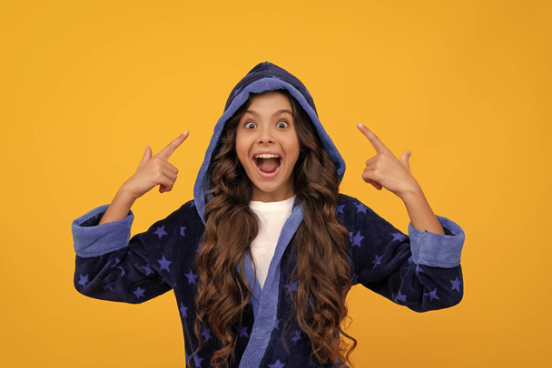 Excited child in hooded bathrobe happy screaming pointing fingers yellow background, point. - Foto, imagen