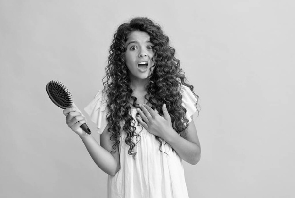 shocked teen girl with long curly hair holding comb hairbrush for combing, daily habits. - Foto, Imagem