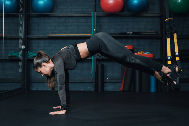 atleta menina está exercitando trx no ginásio. fundo escuro - Foto, Imagem