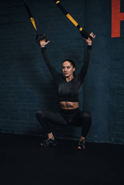 girl athlete is exercising trx in the gym. dark background - Foto, immagini