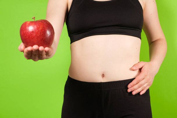 Жінка на зеленому тлі тримає червоне яблуко в руці. Концепція правильного харчування, травлення, дієти з фруктами або сирого харчування
. - Фото, зображення