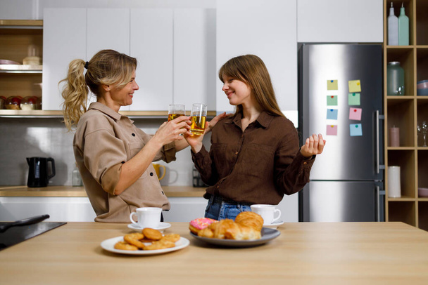 Mom and daughter talk about personal things drink juice and eat sweets in the kitchen - Photo, Image