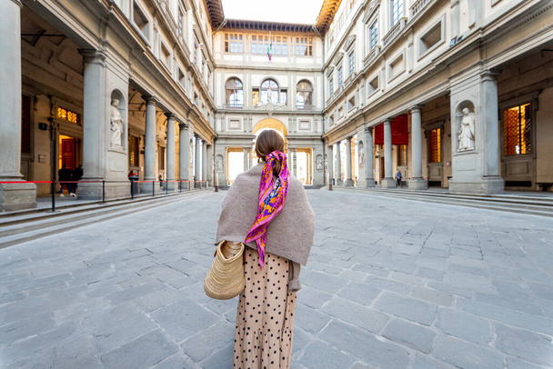 Νεαρή γυναίκα απολαμβάνει αρχιτεκτονική στην πλατεία Uffizi επισκέπτονται μουσείο στη διάσημη ιταλική πόλη της Φλωρεντίας. Γυναικεία τουριστικά ταξίδια ιταλικά αξιοθέατα. Γυναίκα ντυμένη στα ιταλικά με πολύχρωμο μαντήλι στα μαλλιά - Φωτογραφία, εικόνα