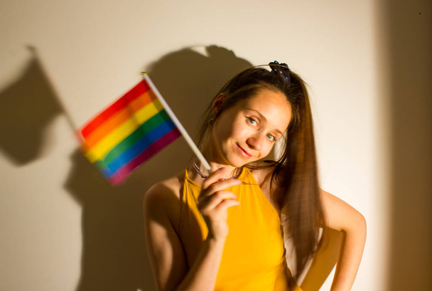 Güzel bir genç kadın, LGBT bayrağını elinde tutan bir kız Onur Ayı 'nı kutluyor. Sevimli seksi kız eğleniyor, gülümsüyor, gülüyor. Gökkuşağı bayrağı - lezbiyenlerin, biseksüellerin, panseksüellerin, eşcinsellerin bulanık fotoğraflarının sembolü - Fotoğraf, Görsel