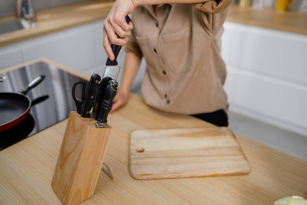 Knifes in wooden block at kitchen. Woman chooses the right knife from the set - Photo, image