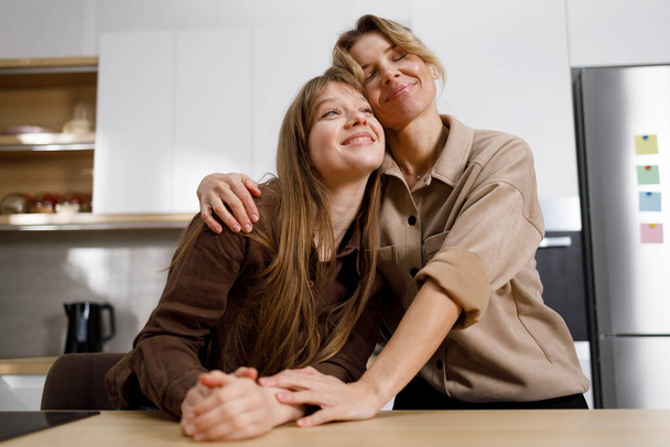 Onnellinen äiti ja hänen aikuinen tyttärensä halaavat keittiössä - Valokuva, kuva