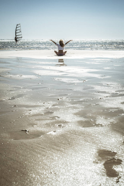 Счастье и свобода концепции образа жизни. Обратный вид женщины, сидящей на песке с океаном вокруг, открывающей руки с удовлетворением и радостью. Женщины наслаждаются летними каникулами - Фото, изображение