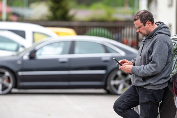 man with smartphone standing next to the car, using mobile app for online communication, shpping - Foto, Bild